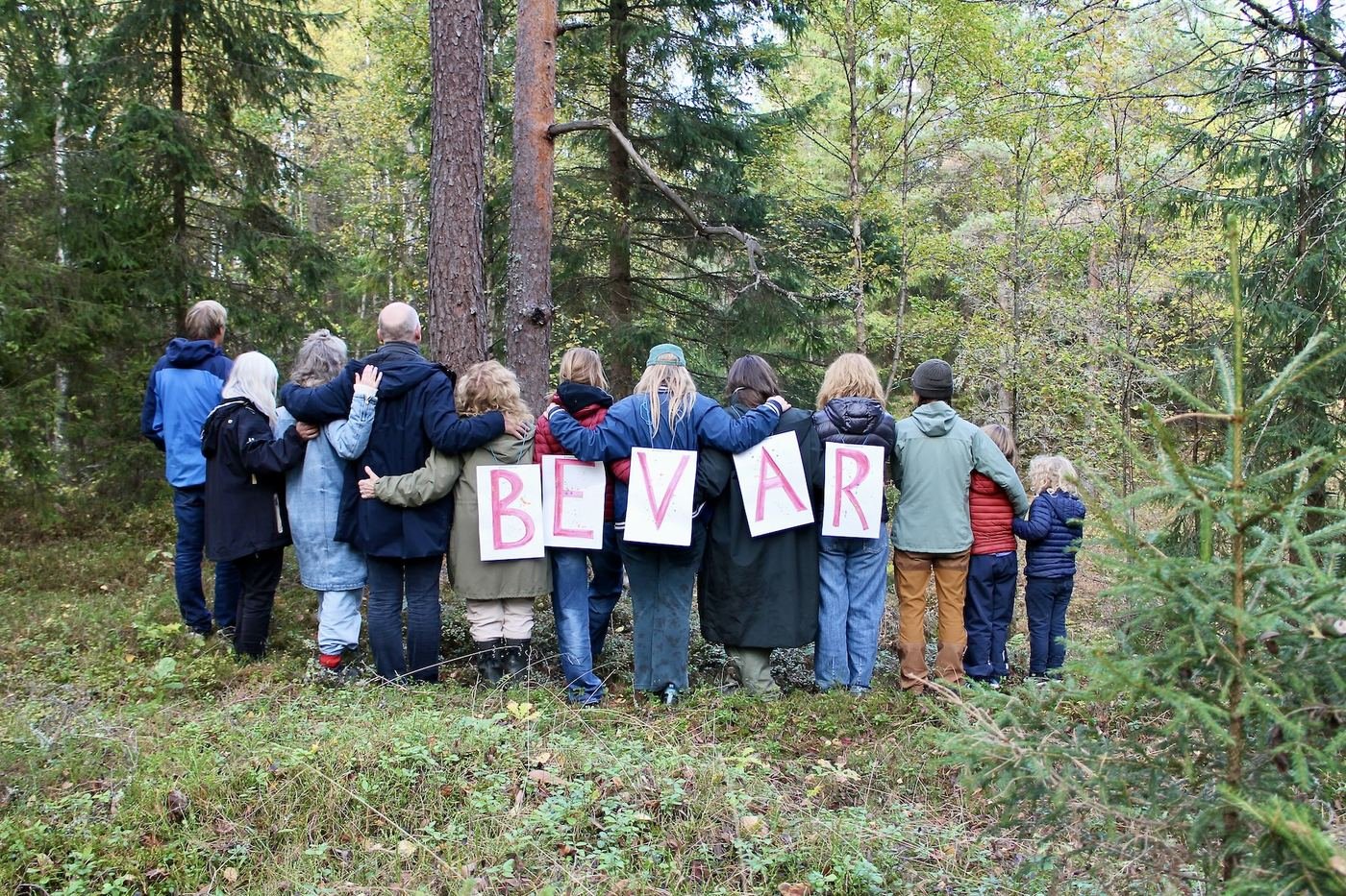 Deltakerne står med ryggen til kamera i skogkanten og holder opp bokstaver som danner ordet BEVAR.